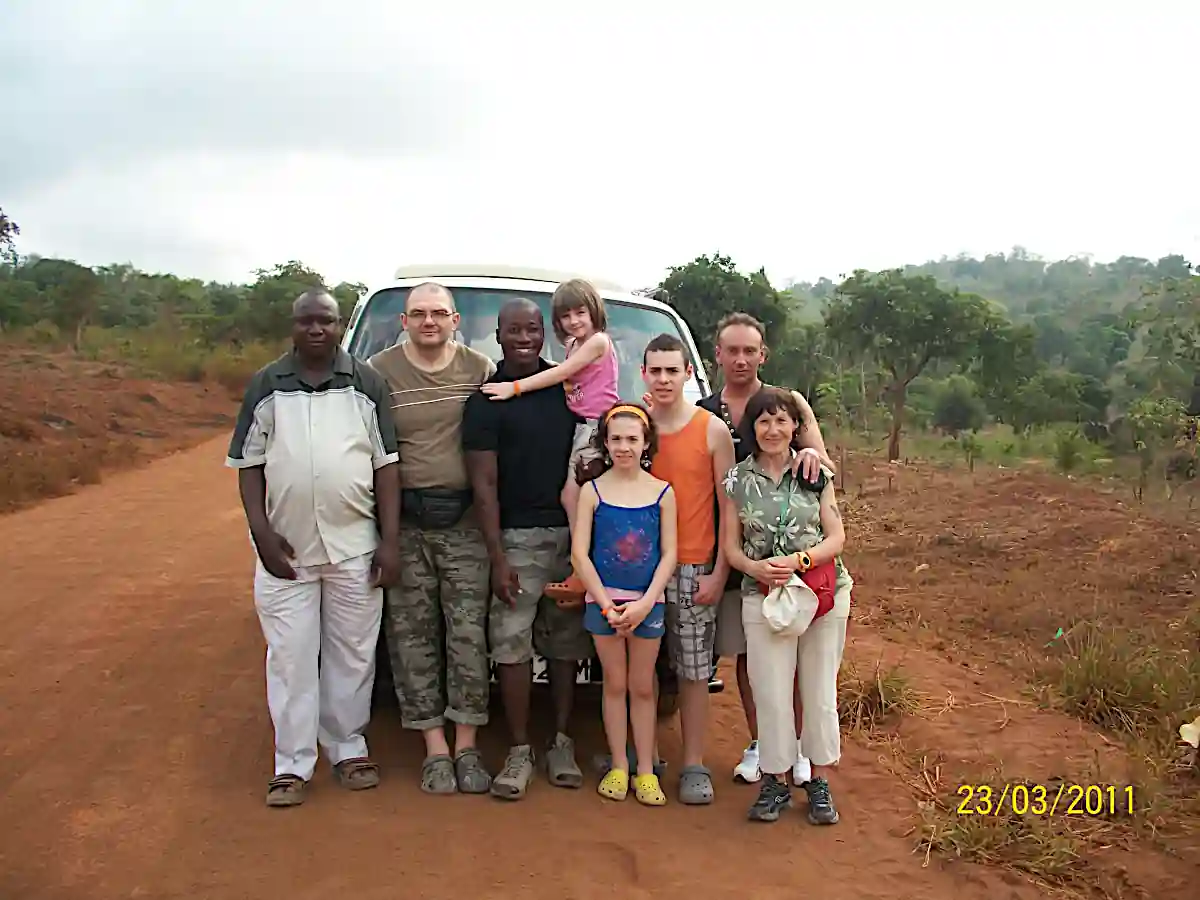 Safari familiare nello Tsavo con Wilderness 360: Morris tiene in braccio la figlia più piccola accanto al pulmino, con la famiglia sorridente nella terra rossa della savana.