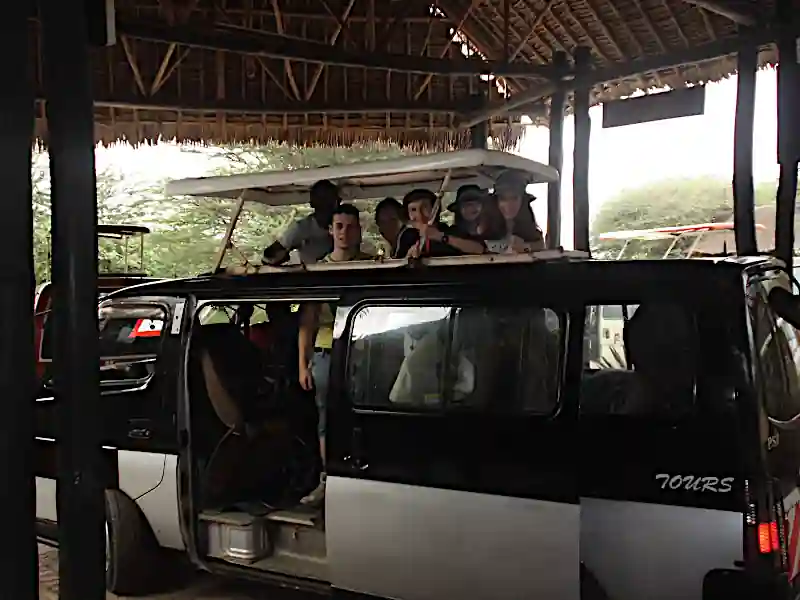 Famiglia felice con bambini in piedi con la testa fuori dal tetto apribile di un pulmino da safari durante un game drive in Kenya con Wilderness 360.